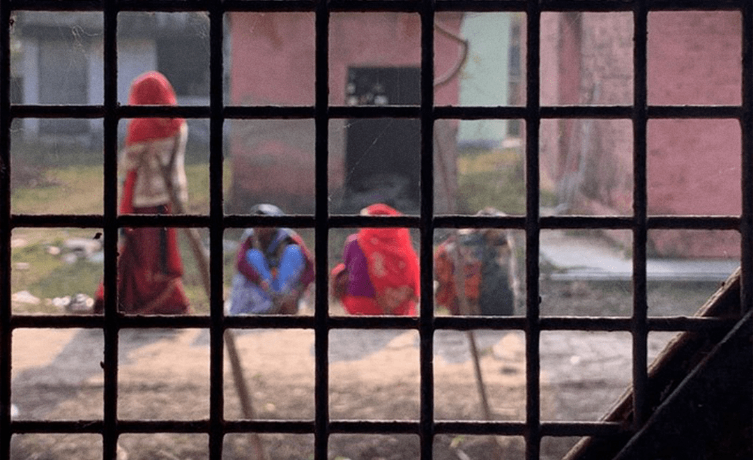 Image has multiple women in an Indian village sitting on the floor viewed through a window to highlight the Long-form Reportage on Women’s Health for PARI