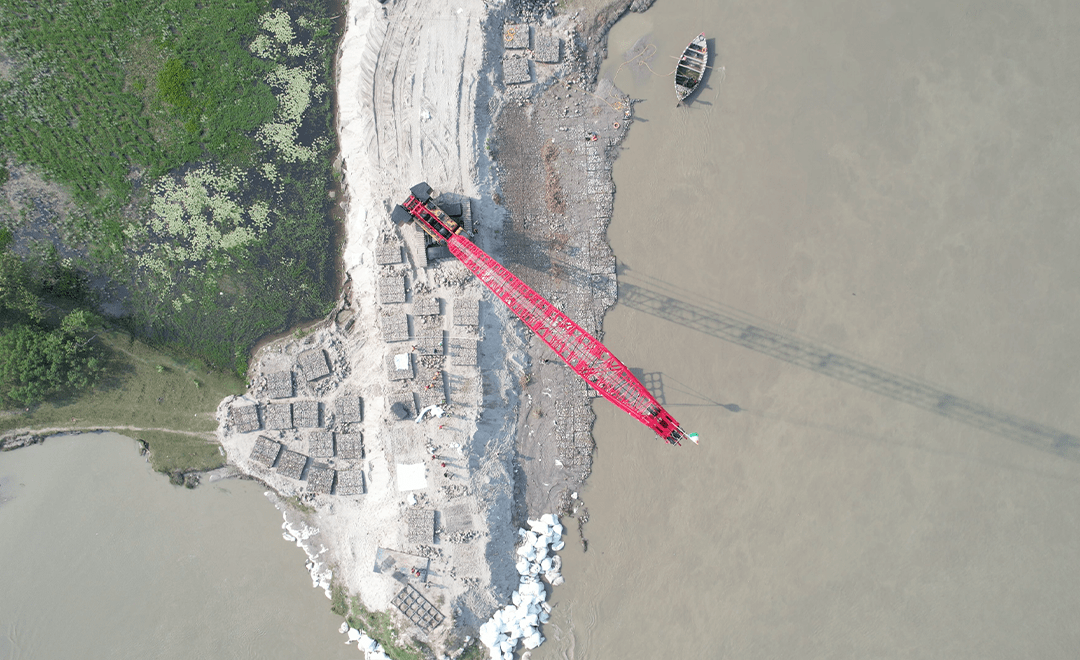 A top-down drone image which has a red crane working at the edge of a waterbody