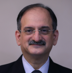An image of a man who identifies as Nozer Sheriar - wearing a suit and tie with glasses and a moustache looking into the camera